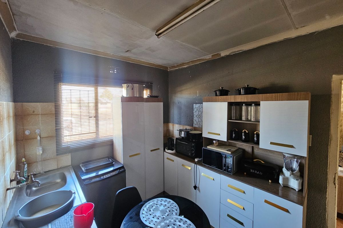 A functional kitchen featuring built-in cabinetry, a double bowl stainless steel sink, and tiled splashbacks, currently requiring ceiling and wall finishing.