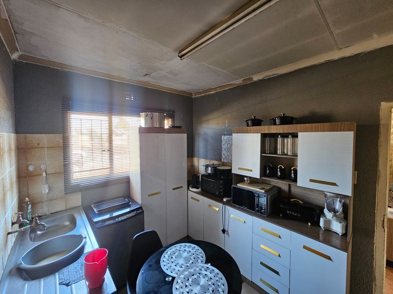 A functional kitchen featuring built-in cabinetry, a double bowl stainless steel sink, and tiled splashbacks, currently requiring ceiling and wall finishing.