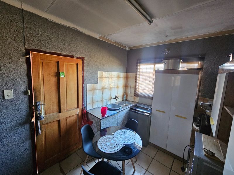 A compact kitchen area featuring a stainless steel sink, tiled splashback, and tiled flooring, requiring cosmetic updates to improve its overall condition and appeal.