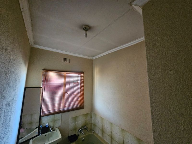 A dated bathroom featuring a bathtub, basin, and tiled splashback, requiring cosmetic updates and modernization to improve its overall condition and appeal.
