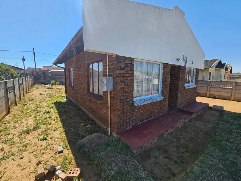 Rear view of a face brick house featuring a concrete parapet, aluminum windows, and a small concrete porch set within a large, undeveloped yard area.