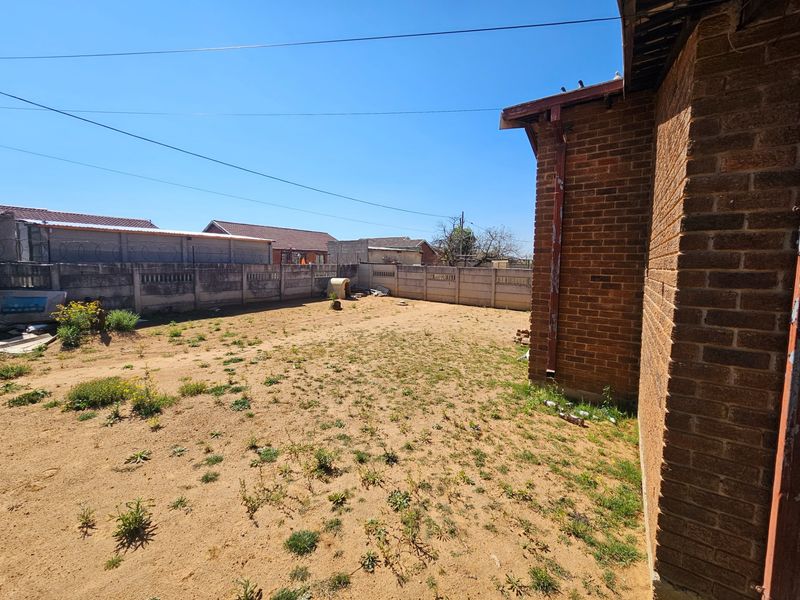 A spacious rear yard featuring a brick exterior wall, precast concrete boundary fencing, and an open area with potential for landscaping.