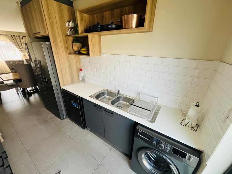 Modern scullery featuring sleek dark cabinetry, white subway tile backsplash, double stainless steel sink, and integrated appliances with clean tiled flooring.