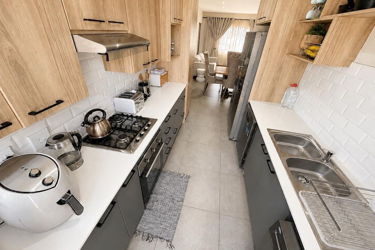 Modern galley-style kitchen featuring light wood cabinetry, stone countertops, subway tile backsplash, gas hob, and integrated oven with a clean, contemporary finish.