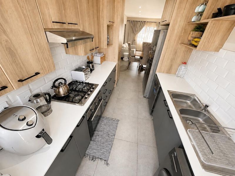 Modern galley-style kitchen featuring light wood cabinetry, stone countertops, subway tile backsplash, gas hob, and integrated oven with a clean, contemporary finish.