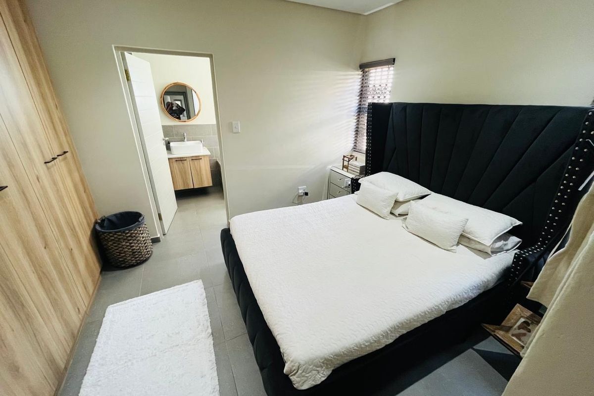 A well-maintained bedroom featuring built-in wardrobes, tiled flooring, and an en-suite bathroom with a modern vanity and mirror.