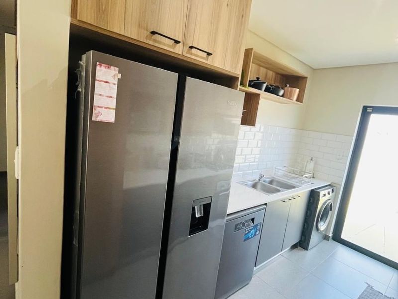 A modern scullery featuring wood-finish cabinetry, subway tile backsplash, double basin sink, and tiled flooring with integrated appliance spaces.