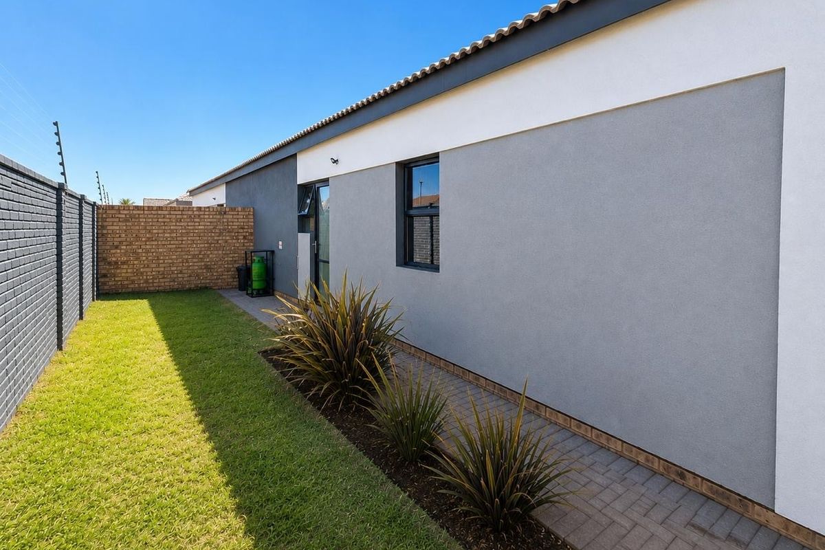 A well-maintained rear exterior view featuring a paved walkway, manicured lawn, brick boundary wall, and secure electric fencing.
