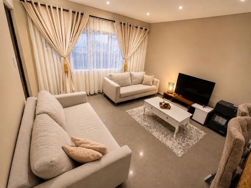 A well-maintained living room featuring neutral tiled flooring, recessed downlighting, and large windows fitted with security bars.