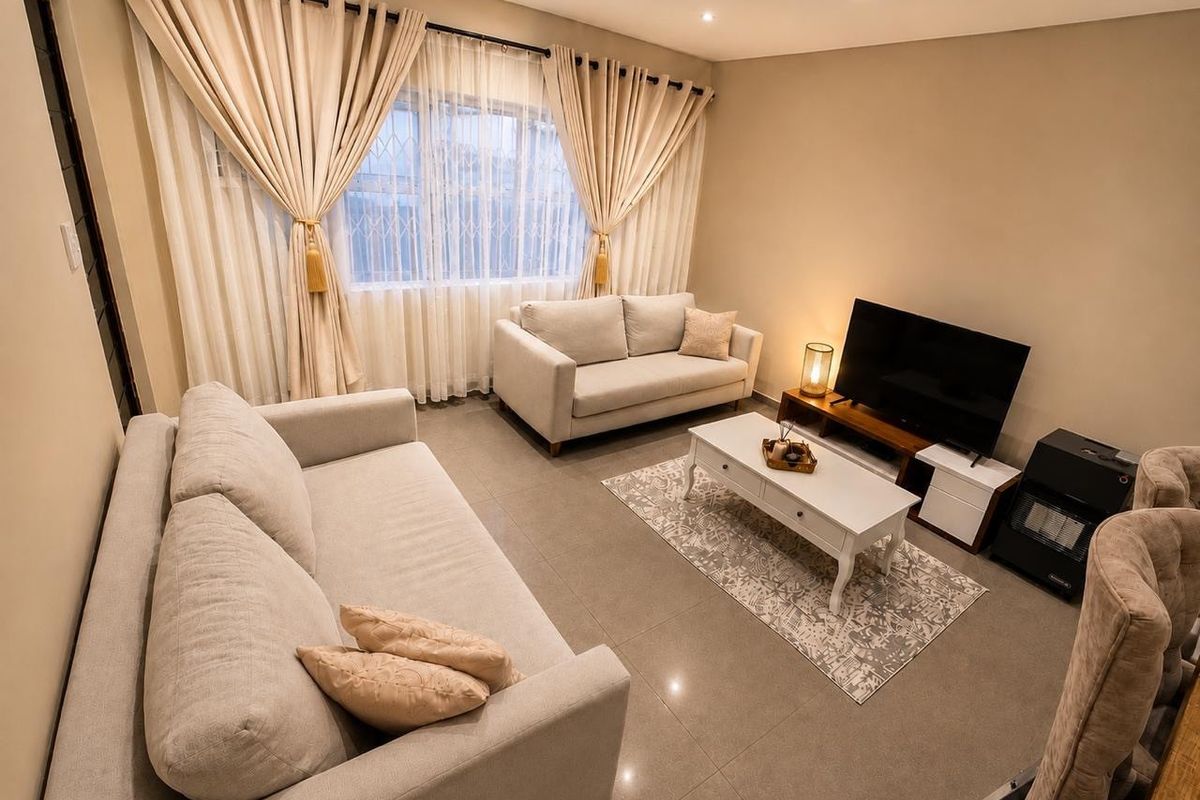 A well-maintained living room featuring neutral tiled flooring, recessed downlighting, and large windows fitted with security bars.