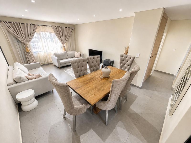 An open-plan living and dining area featuring neutral tiled flooring, recessed downlighting, and a clean, modern aesthetic with a built-in storage cupboard.
