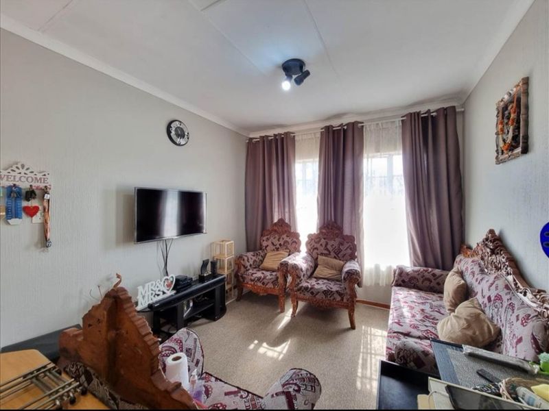 A cozy living room featuring neutral wall finishes, carpeted flooring, and large windows with installed curtain rails.