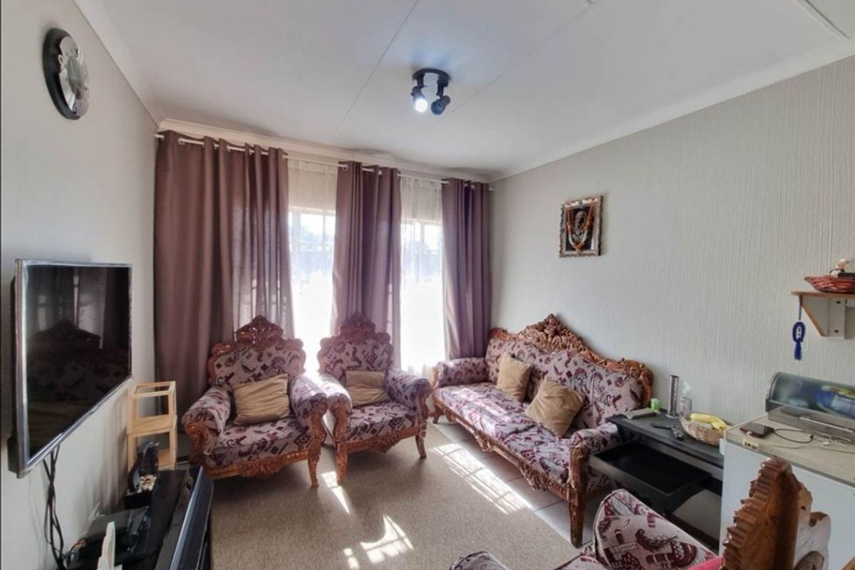 A comfortable living room featuring neutral wall finishes, carpeted flooring, and natural light provided by a large window with installed curtain tracks.