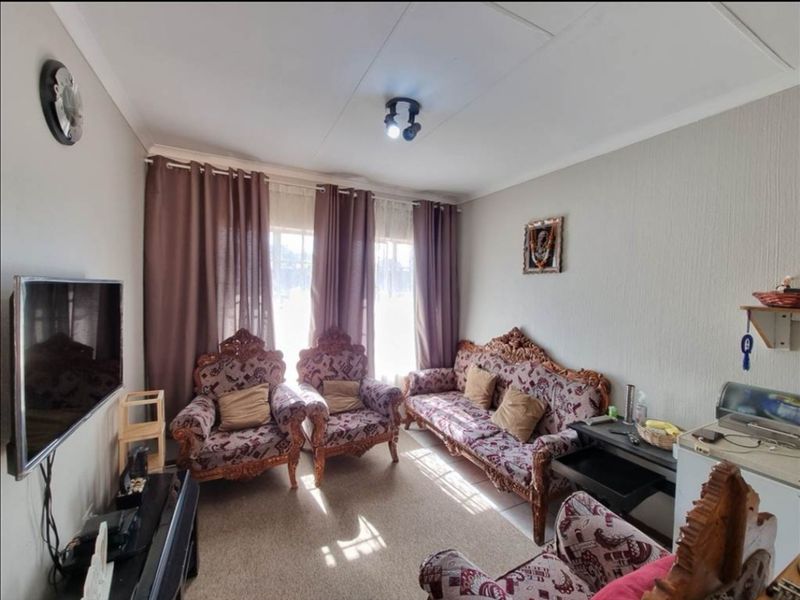 A comfortable living room featuring neutral wall finishes, carpeted flooring, and natural light provided by a large window with installed curtain tracks.