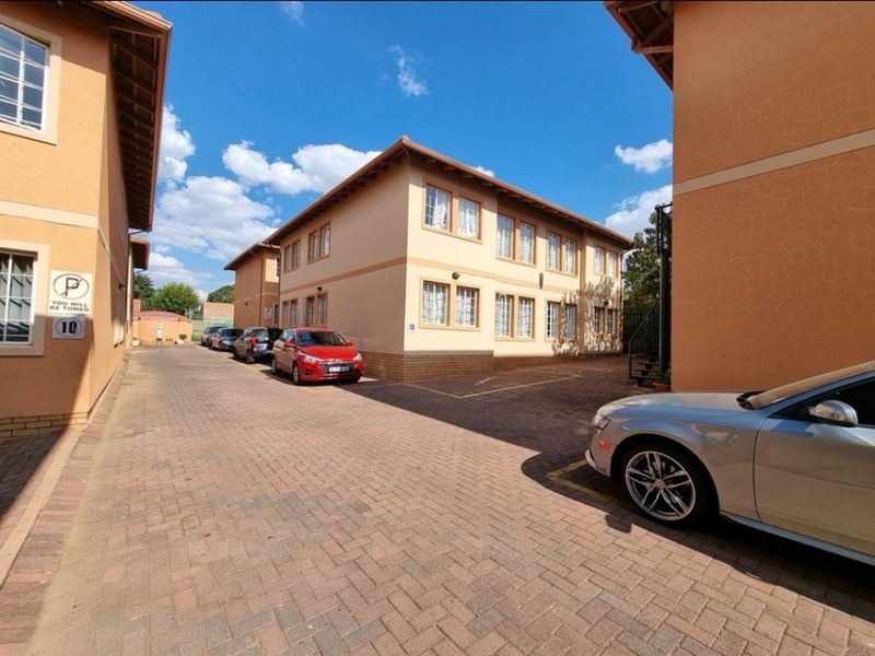 Exterior view of a multi-story townhouse complex featuring a paved driveway and designated parking areas.