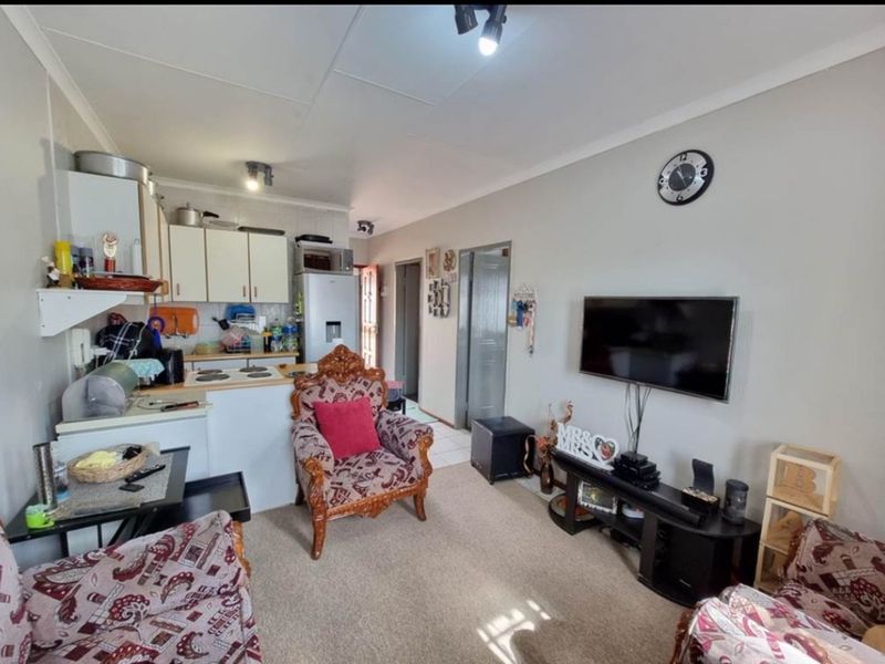 Open-plan living area featuring a compact kitchen with built-in cabinetry and electric hob, seamlessly flowing into the lounge space.