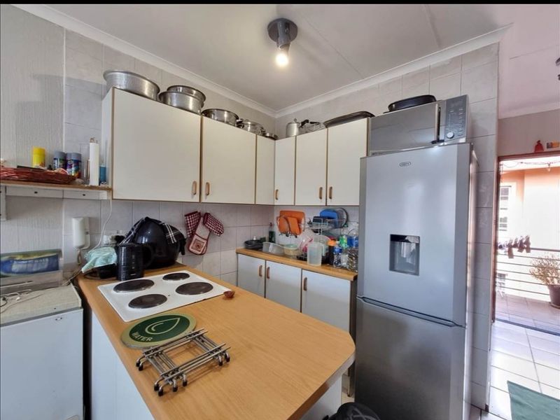 A compact kitchen featuring white cabinetry, a laminate countertop, and an electric hob, with tiled splashbacks and direct access to an outdoor area.
