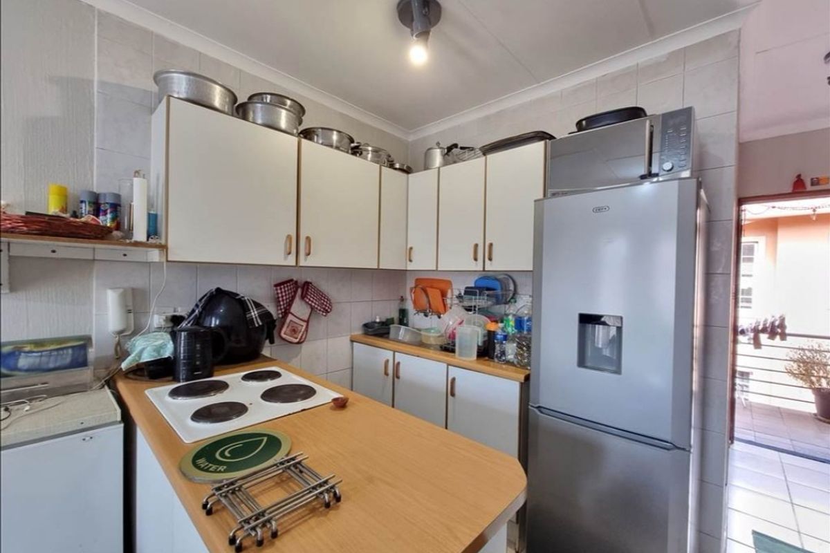 A compact kitchen featuring white cabinetry, a laminate countertop, and an electric hob, with tiled splashbacks and direct access to an outdoor area.