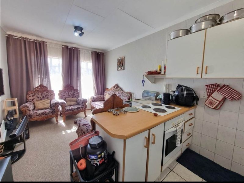 Open-plan living area featuring a compact kitchen with electric hob, built-in oven, and tiled backsplash, seamlessly connected to a carpeted lounge space.