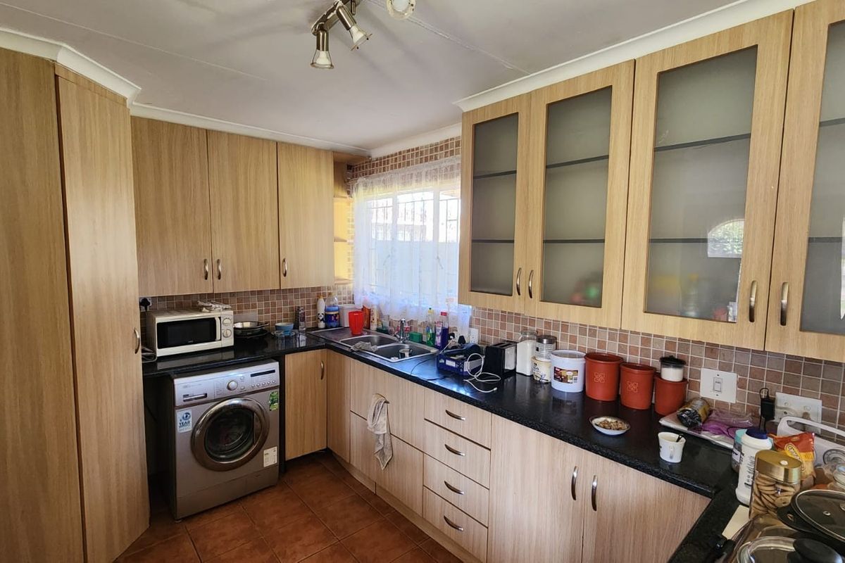 Functional kitchen featuring light wood-finish cabinetry, granite countertops, tiled backsplash, and integrated laundry facilities with ample storage space.
