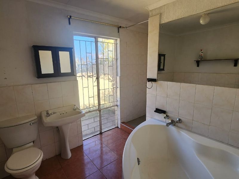 A dated bathroom featuring a pedestal basin, toilet, and built-in bathtub with tiled finishes and direct access to the exterior via a security gate.