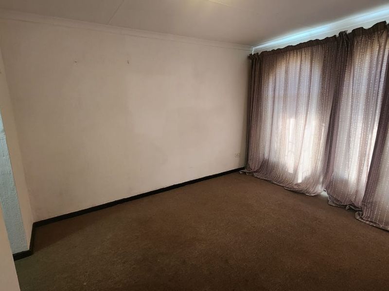 An empty bedroom featuring carpet flooring and large window curtains, presenting a blank canvas ready for renovation or new interior design.