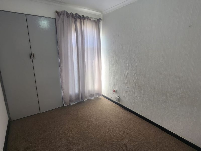 A compact, empty bedroom featuring a built-in wardrobe, carpeted flooring, and neutral wall finishes, ready for personalization.