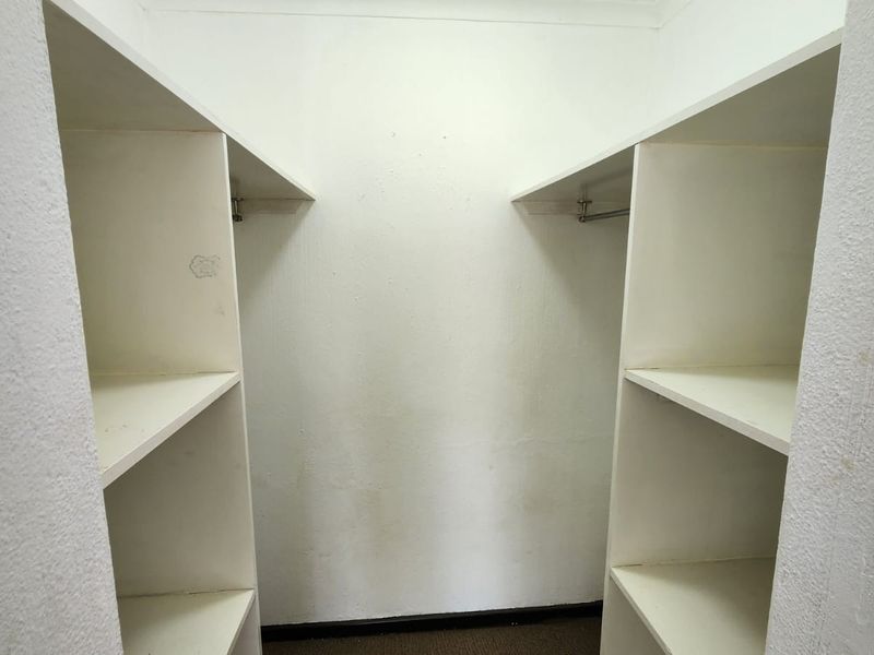 A walk-in closet space featuring built-in white shelving and hanging rails, currently empty and showing signs of wear on the walls.