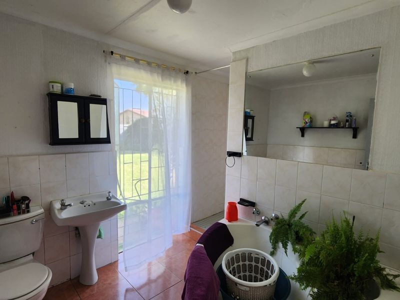 A dated bathroom featuring a pedestal basin, toilet, and built-in bathtub with tiled finishes and direct access to the garden via a security gate.