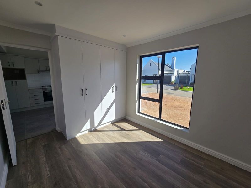 A bright, modern bedroom featuring neutral walls, durable laminate flooring, and ample built-in cupboard space, with a view towards the street.