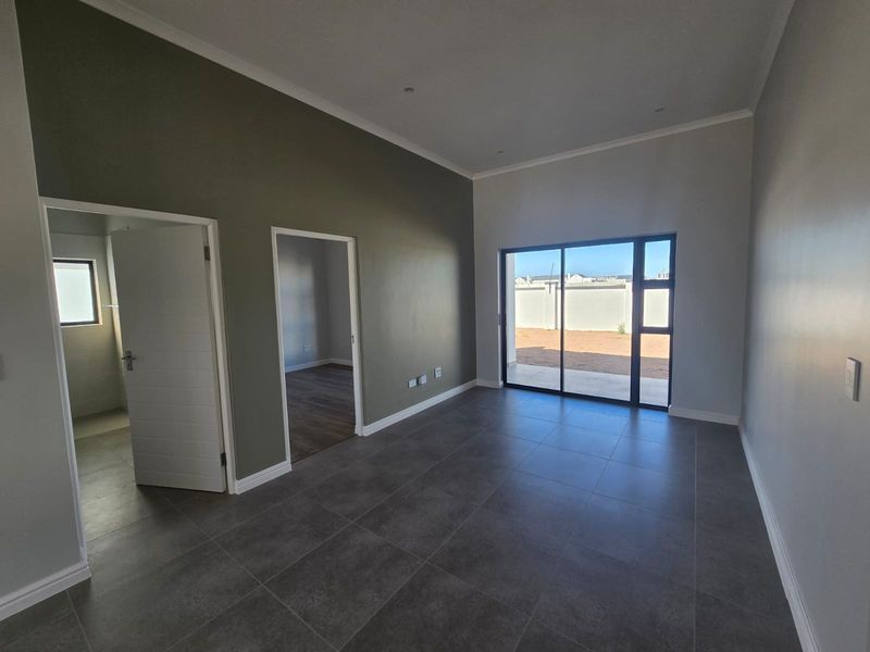 A bright, modern, and empty living area featuring large format floor tiles, neutral walls, and a sliding glass door leading to the rear exterior.