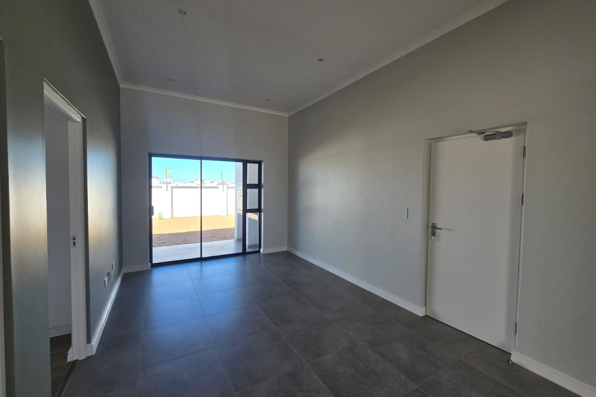 A bright, empty living room featuring modern tiled flooring, recessed downlights, and a large sliding glass door providing access to the rear exterior.
