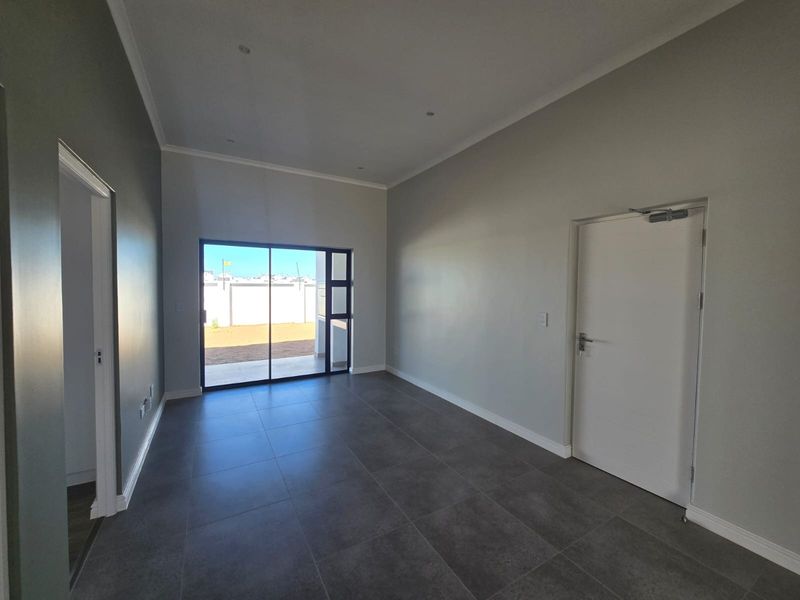 A bright, empty living room featuring modern tiled flooring, recessed downlights, and a large sliding glass door providing access to the rear exterior.