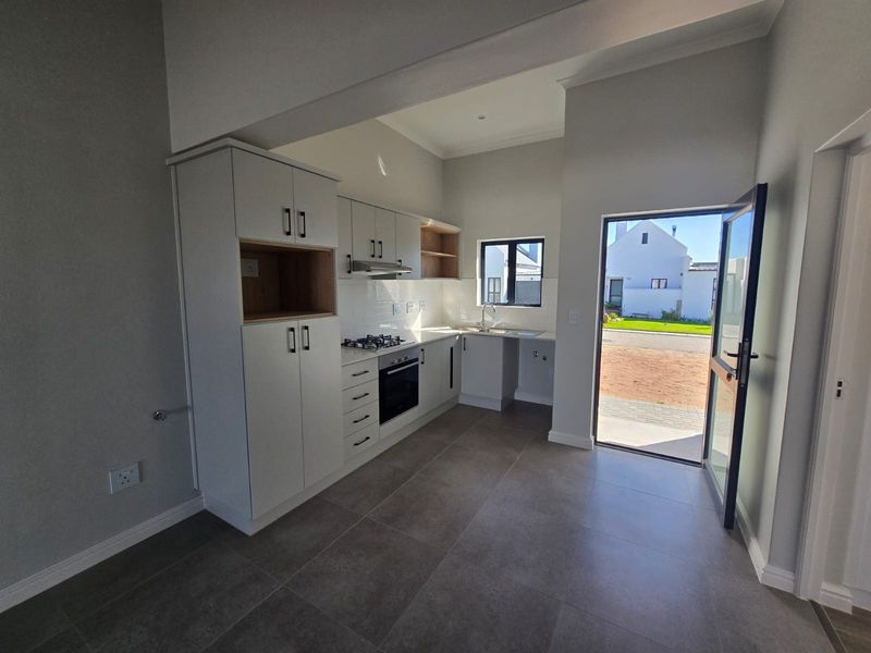 Modern kitchen featuring sleek white cabinetry, built-in gas hob, electric oven, and tiled flooring, with direct access to the exterior.