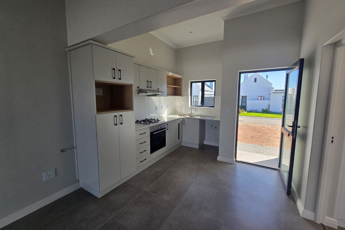 Modern kitchen featuring sleek white cabinetry, built-in gas hob, electric oven, and tiled flooring, with direct access to the exterior.