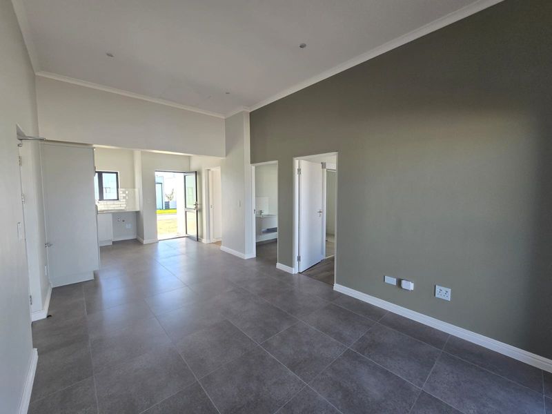 Spacious open-plan living area featuring modern grey floor tiles, neutral wall tones, and recessed lighting, seamlessly connecting to the kitchen and exterior access.