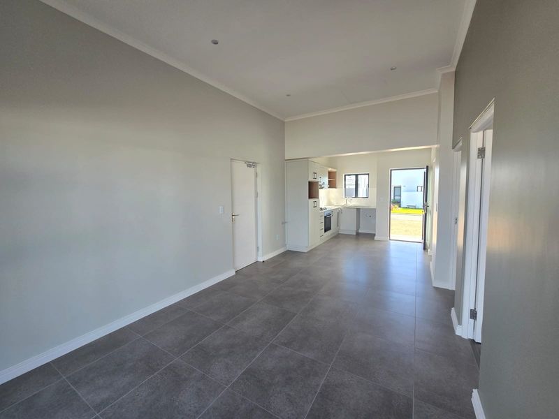 Spacious open-plan living area featuring modern grey floor tiles, recessed lighting, and a clean, functional kitchen with built-in appliances and direct outdoor access.