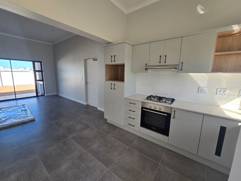Modern open-plan kitchen and living area featuring sleek cabinetry, built-in appliances, subway tile backsplash, and large sliding doors leading to the exterior.