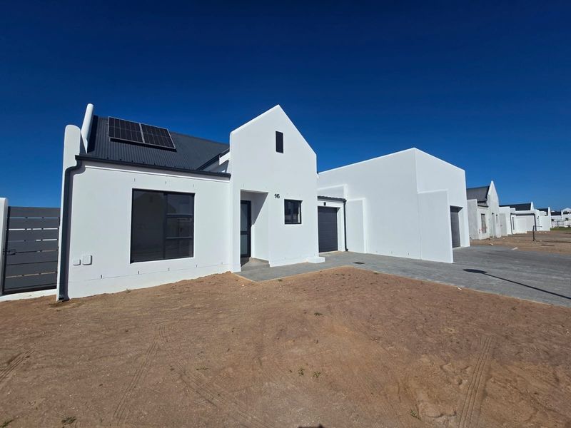 Modern single-story house featuring a clean white facade, metal roof with solar panels, integrated garage, and a paved driveway in a new development.