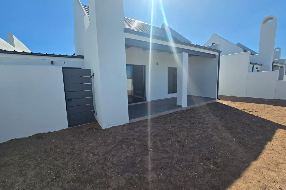 Rear view of a modern house featuring a covered patio, sliding glass doors, and an unlandscaped garden area.