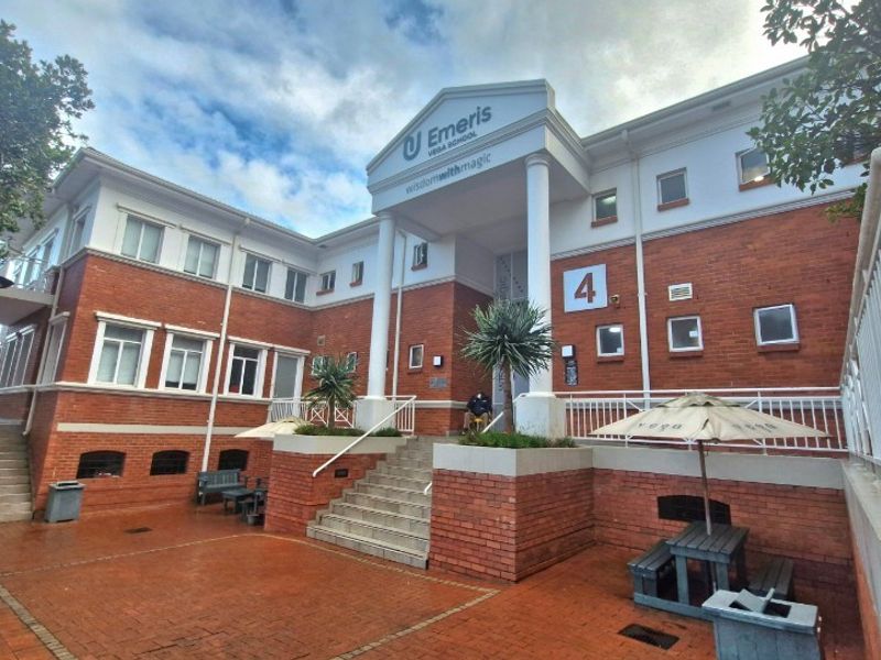 Front elevation of a multi-story brick office building featuring a prominent entrance with classical columns and a paved courtyard area.