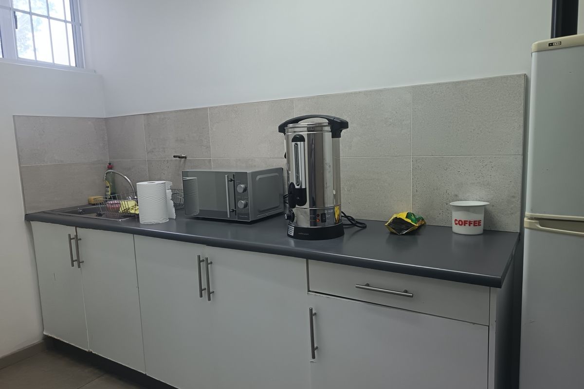 A functional office kitchenette featuring white cabinetry, a dark laminate countertop, a stainless steel sink, and neutral tiled backsplash.