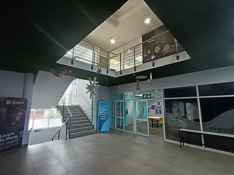 Spacious office building entrance featuring a central staircase, mezzanine level, and modern glass partitioning, creating an open and airy reception area.