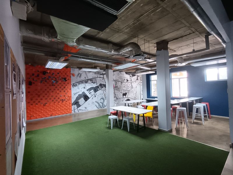 Open-plan office space featuring an industrial aesthetic with exposed concrete ceilings, ductwork, and a mix of artificial turf and polished concrete flooring.