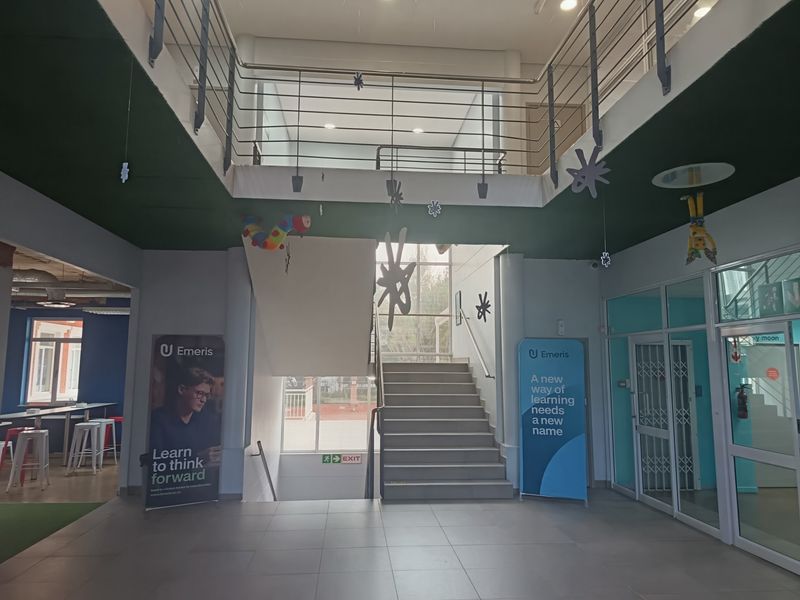 Spacious office building entrance foyer featuring a central staircase, mezzanine level, and modern tiled flooring with glass partition access.
