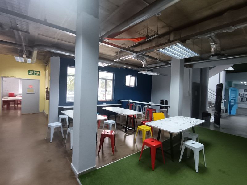 Open-plan office space featuring an industrial aesthetic with exposed ceilings, ducting, and a mix of vinyl and artificial turf flooring.