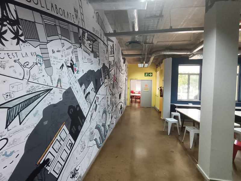 A creative office hallway featuring an extensive wall mural, exposed industrial ceiling ducting, and polished concrete flooring in a modern workspace environment.
