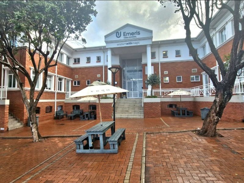Front exterior view of the office building featuring a brick facade, central entrance with columns, and a paved courtyard area.