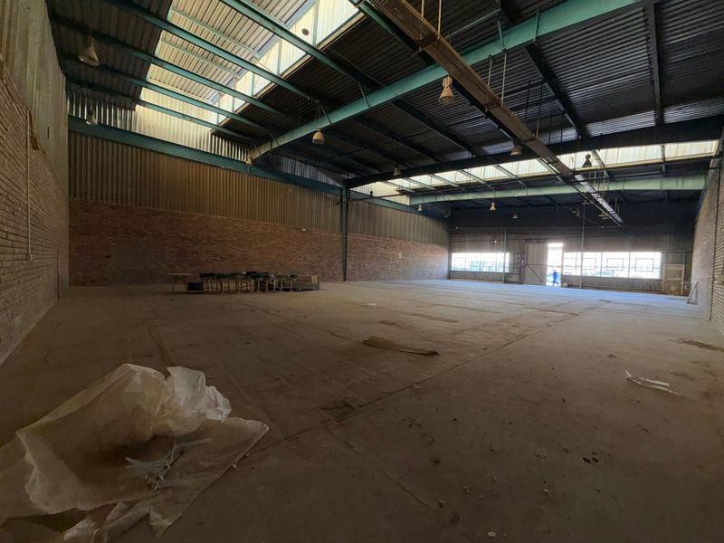 Spacious industrial warehouse featuring exposed brick walls, high steel truss ceilings with integrated skylights, and durable concrete flooring, suitable for various commercial or storage uses.