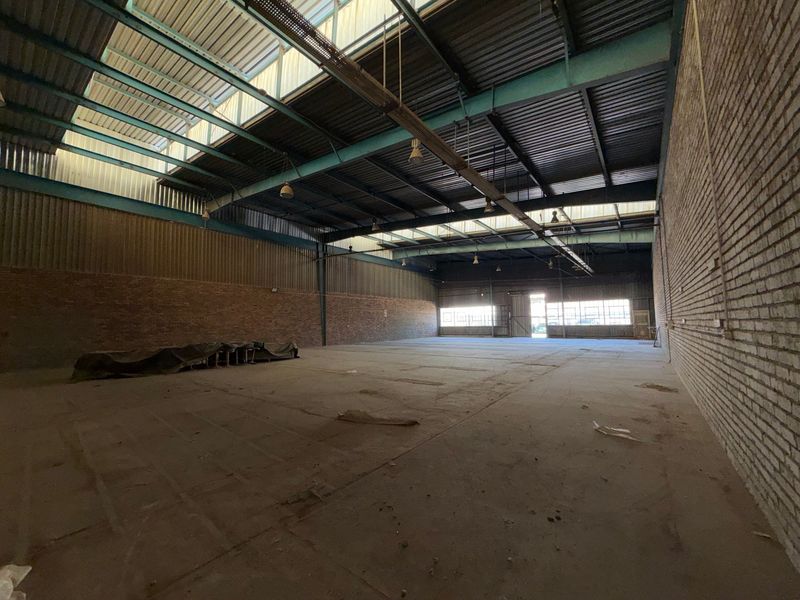 Spacious industrial warehouse featuring exposed brick walls, high steel truss ceilings with integrated skylights, and durable concrete flooring.
